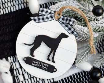 Può includere: Ciondolo in legno bianco con una silhouette nera di un levriero e il nome "Garrison" scritto su un cartellino nero. Il ciondolo è decorato con un nastro a scacchi bianco e nero.