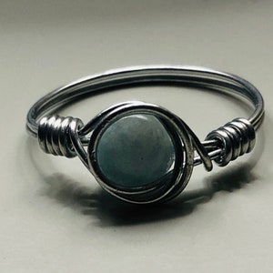 May include: A silver wire wrapped ring with a light blue gemstone.