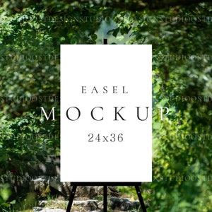 Puede incluir: Una maqueta de caballete blanco con el texto "EASEL MOCKUP 24x36" en él. El caballete está instalado al aire libre en un camino de piedra con vegetación verde en el fondo.
