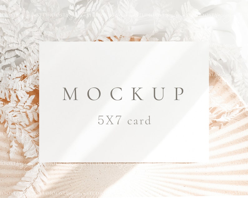 May include: A white card mockup with the text "MOCKUP 5X7 card" on a beige background with white dried ferns.