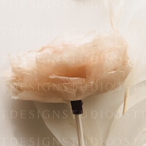 May include: A delicate, blush-colored feather flower on a white stick. The flower is made of soft, fluffy feathers and has a delicate, romantic look.
