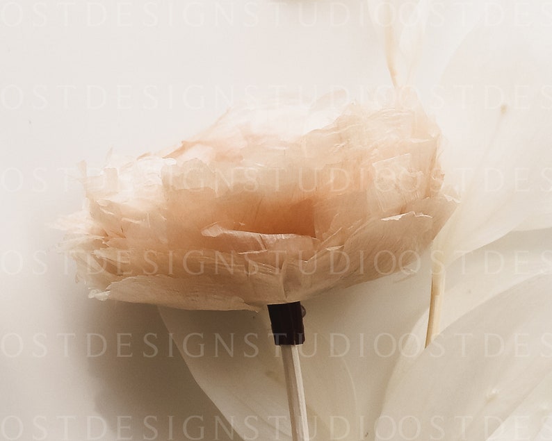 May include: A delicate, blush-colored feather flower on a white stick. The flower is made of soft, fluffy feathers and has a delicate, romantic look.