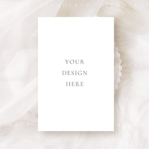 Pode incluir: Um mockup de cart&atilde;o branco com o texto "YOUR DESIGN HERE" em um fundo de tecido branco.