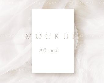May include: A white A6 card mockup on a white textured background. The card is blank and has the word "MOCKUP" and "A6 card" printed on it in a light gray font.