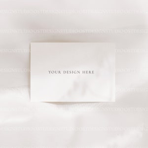Op de afbeelding: Een blanco witte kaart met de tekst "YOUR DESIGN HERE" in zwart gedrukt op een witte stoffen achtergrond.