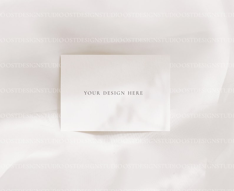 Op de afbeelding: Een blanco witte kaart met de tekst "YOUR DESIGN HERE" in zwart gedrukt op een witte stoffen achtergrond.