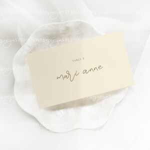 May include: A white card with the text "TABLE 2" and "mari anne" written in gold calligraphy on a white background.
