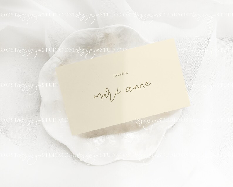 May include: A white card with the text "TABLE 2" and "mari anne" written in gold calligraphy on a white background.