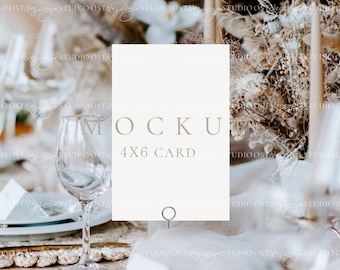May include: A white 4x6 card mockup with the text "MOCKU 4X6 CARD" on a table setting with a wine glass and a bouquet of dried flowers.