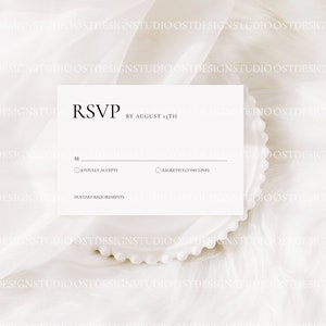 May include: A white RSVP card with black text. The card has a section for the guest's name, a checkbox to accept or decline the invitation, and a space for dietary requirements. The text on the card reads "RSVP by August 15th".