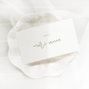 May include: White card with gold text on a white background. The card says "Table 2" and "mari anne".