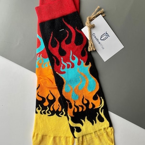 Könnte beinhalten: Ein Paar schwarze Socken mit einem bunten Flammenmuster. Die Flammen sind rot, orange, gelb und blau. Die Socken haben einen gelben Bund und sind aus Baumwolle.