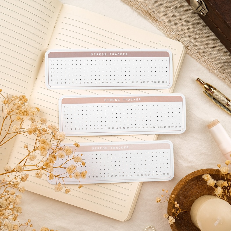 May include: Three stress tracker sheets with a pink and white color scheme. Each sheet has a grid of dots for tracking stress levels. The text "STRESS TRACKER" is printed at the top of each sheet.