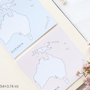 May include: Two square notepads with a map of Oceania, each measuring 3.54 x 3.74 inches. One notepad is light blue, the other is light pink. The word "OCEANIA" is printed on each notepad. Pink flowers are in the background.