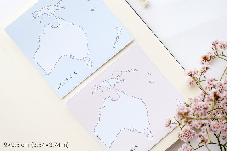 May include: Two square notepads with a map of Oceania, each measuring 3.54 x 3.74 inches. One notepad is light blue, the other is light pink. The word "OCEANIA" is printed on each notepad. Pink flowers are in the background.