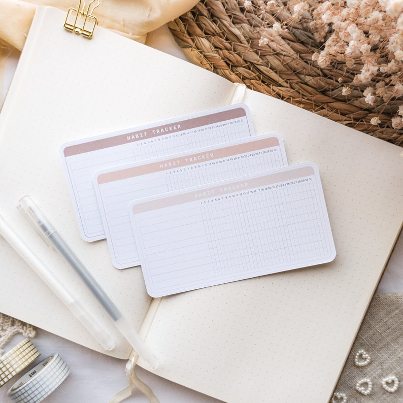 May include: Three habit tracker sheets with a gradient pink and white design. The sheets are labeled "Habit Tracker" and have a grid pattern for tracking daily habits.