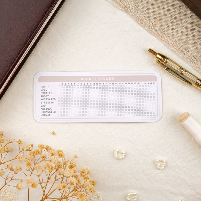 May include: A white mood tracker with a pink header and black text. The tracker has a grid of 31 squares, with each square representing a day of the month. The tracker includes a list of moods: Happy, Upset, Excited, Angry, Motivated, Stressed, Sad, Anxious, Exhausted, and Normal.