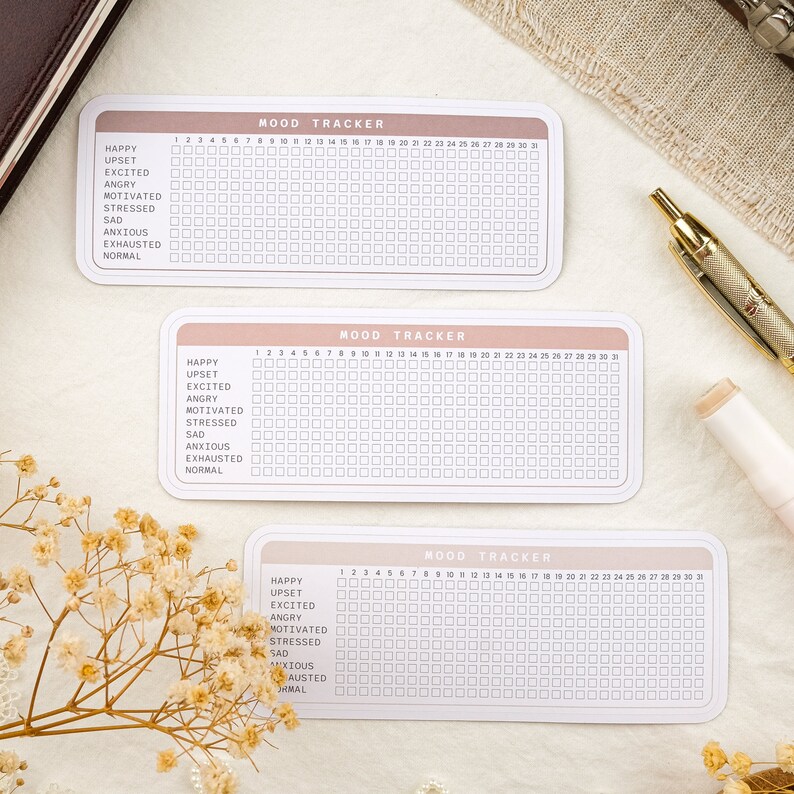 May include: Three printable mood trackers with a pink and white color scheme. Each tracker has a grid with 31 squares for each day of the month. The trackers are labeled "MOOD TRACKER" and list mood options such as "Happy", "Upset", "Excited", "Angry", "Motivated", "Stressed", "Sad", "Anxious", "Exhausted", and "Normal".