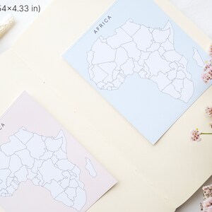 May include: Two square cards, each 3.54 x 4.33 inches, feature a map of Africa with the word "AFRICA" at the top. One card is light blue, the other is light pink. A small glass vial and pink flowers are also in the image.