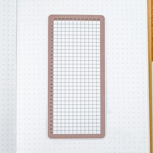 May include: A brown and white monthly calendar sticker with a grid layout and the months of the year listed across the top. The sticker is designed for use in a bullet journal or planner.