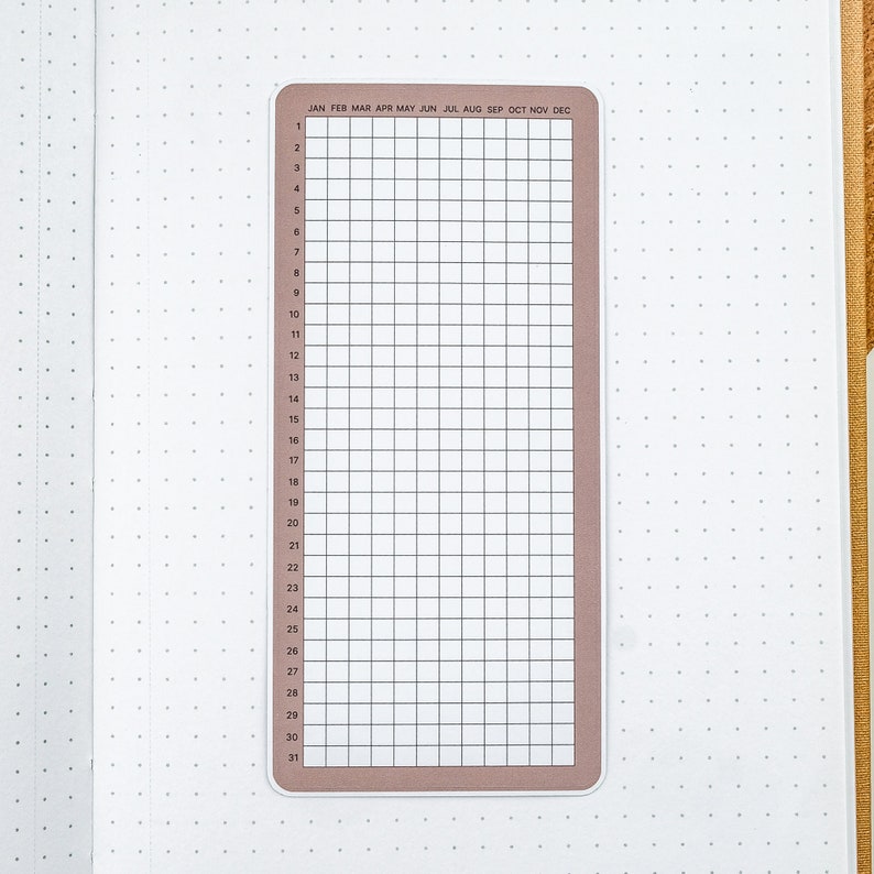 May include: A brown and white monthly calendar sticker with a grid layout and the months of the year listed across the top. The sticker is designed for use in a bullet journal or planner.