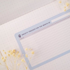 May include: A blue and white anxiety tracker for the month of. The tracker has a grid with numbers 1 through 28 and the word "SYMPTOMS" at the top.