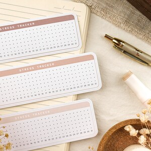 May include: Three pink and white stress tracker cards with black dots. Each card has the text "STRESS TRACKER" and numbers 1-31.