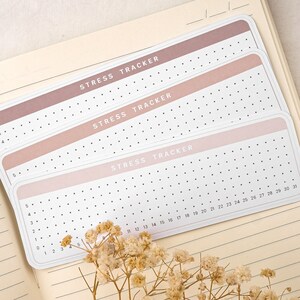 May include: Three pink and white stress tracker sheets with black dots and the text "Stress Tracker" printed on each sheet. The sheets are numbered from 0 to 31.