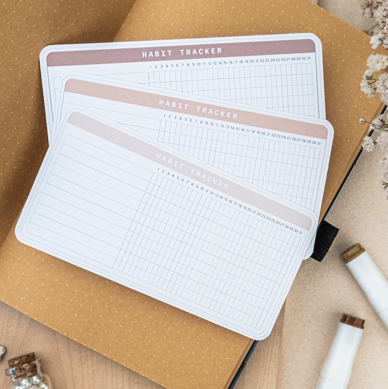 May include: Three white habit trackers with a light pink gradient on the top. Each tracker has a grid with numbers 1 through 31 for the days of the month. The text "HABIT TRACKER" is printed at the top of each tracker.
