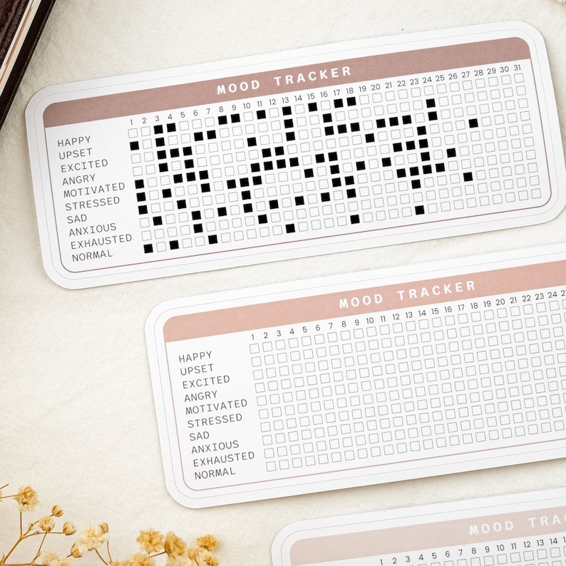 May include: A mood tracker with a pink and white color scheme. The tracker has a grid of squares with numbers 1 through 31 at the top. The left side of the tracker lists mood options: Happy, Upset, Excited, Angry, Motivated, Stressed, Sad, Anxious, Exhausted, and Normal.