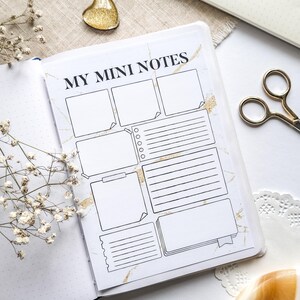 May include: Open notebook with the text "MY MINI NOTES" on a white page with a marble design and gold accents. The page has boxes and lines for notes. A gold heart-shaped object and scissors are also visible.