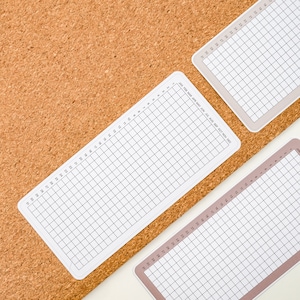 May include: Two white gridded sheets of paper with month names printed on the top sheet. The sheets are on a brown corkboard background.