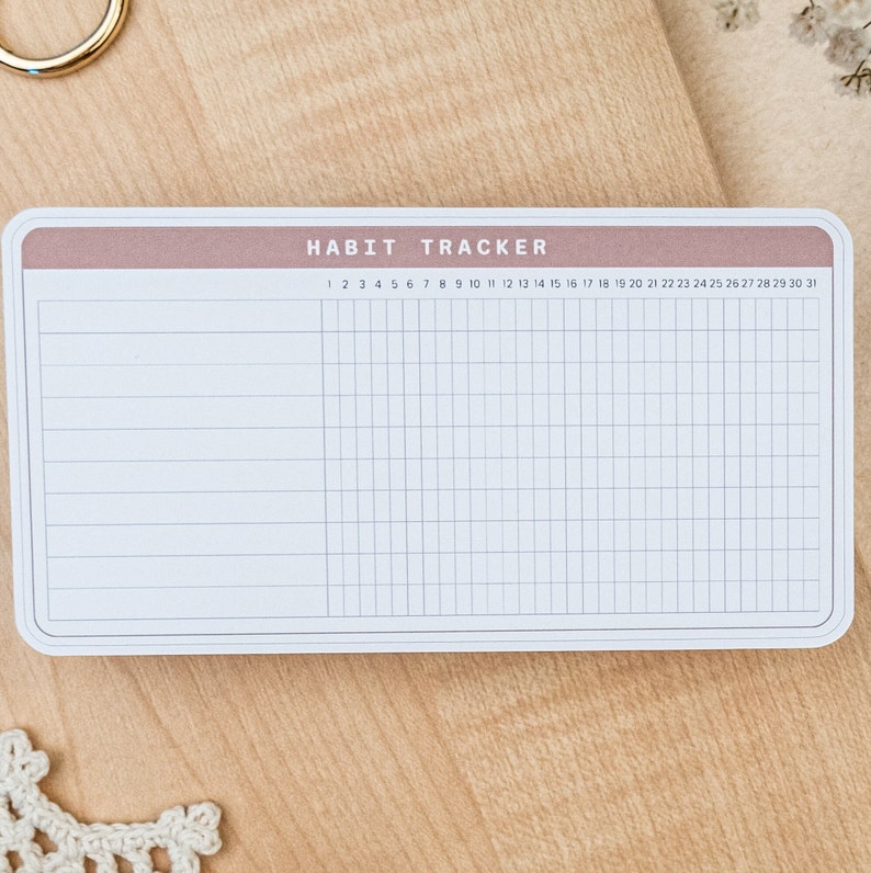 May include: A white habit tracker with a light brown header. The header has the text "HABIT TRACKER" in black. The tracker has 31 columns for each day of the month and 10 rows for tracking habits.