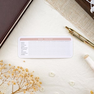 May include: A pink and white mood tracker with a grid of 31 squares for each day of the month. The tracker includes a list of moods: happy, upset, excited, angry, motivated, stressed, sad, anxious, exhausted, and normal.