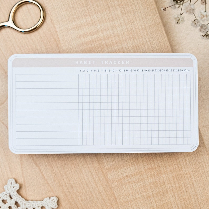 May include: A white habit tracker with a light brown border. The tracker has a grid of squares with numbers 1 through 31 printed at the top.