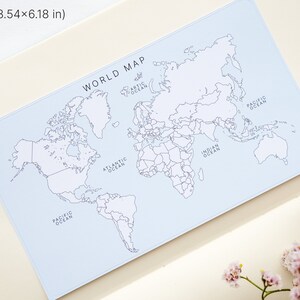 May include: A light blue world map, measuring 3.54 x 6.18 inches, with continents outlined in black. The map is labeled "WORLD MAP" and includes the names of the oceans. The image also features a small glass vial and pink flowers.