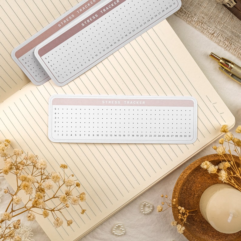 May include: A pink and white printable stress tracker with a grid of dots and numbers 1-30. The text "Stress Tracker" is printed at the top of the tracker.