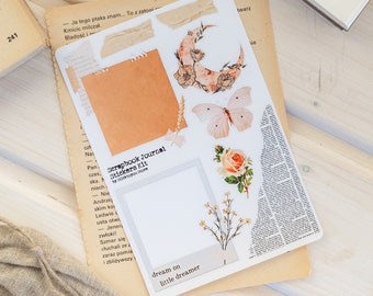 May include: A sheet of scrapbook journal stickers with a variety of designs, including a crescent moon with flowers, a butterfly, a floral arrangement, and a blank photo frame. The stickers are printed on white paper and have a matte finish. The text "Scrapbook Journal Stickers Kit" is printed on the sheet.
