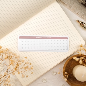 May include: A pink and white stress tracker with a grid of dots for marking stress levels. The tracker has the text "Stress Tracker" printed on it.