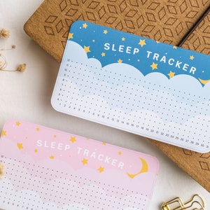 Może przedstawiać: Dwa śledzące sen w pastelowych kolorach z motywem księżyca i gwiazd. Śledzące są oznaczone jako "SLEEP TRACKER" i mają siatkę do zaznaczania godzin snu.