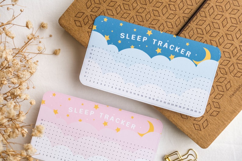 Może przedstawiać: Dwa śledzące sen w pastelowych kolorach z motywem księżyca i gwiazd. Śledzące są oznaczone jako "SLEEP TRACKER" i mają siatkę do zaznaczania godzin snu.
