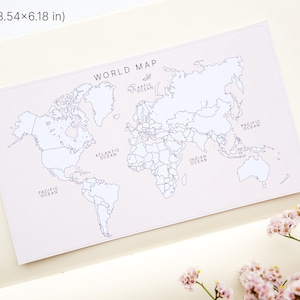 May include: A rectangular world map print, 3.54 x 6.18 inches, with continents and oceans labeled in black on a pale pink background. The words "WORLD MAP" are at the top. The map is set on a cream-colored notebook page.