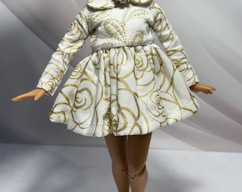 Può includere: Un vestito bianco con un motivo a rose dorate e un colletto bianco. Il vestito ha una spilla gioiello sul décolleté.