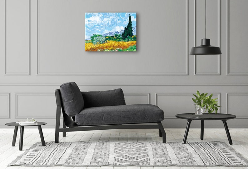May include: A painting of a field of yellow flowers with a single cypress tree in the background. The sky is blue with white clouds. The painting is in a modern living room setting with a gray couch and a black side table.