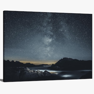 May include: A night sky filled with stars, including the Milky Way, over a mountain range. The mountains are silhouetted against the sky, and there is a layer of clouds in the valley below.