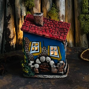 Puede incluir: Una peque&ntilde;a casa de cer&aacute;mica azul y roja con chimenea, ventanas y una fachada de piedra. La casa est&aacute; decorada con detalles amarillos y tiene una peque&ntilde;a puerta.