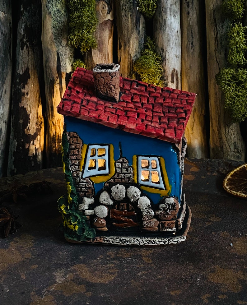 Puede incluir: Una peque&ntilde;a casa de cer&aacute;mica azul y roja con chimenea, ventanas y una fachada de piedra. La casa est&aacute; decorada con detalles amarillos y tiene una peque&ntilde;a puerta.