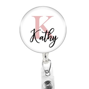 May include: A white badge holder with a pink letter K and the name Kathy in black script.