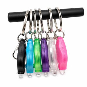 May include: A collection of colorful LED keychain flashlights. The flashlights are in black, blue, green, purple, clear, and pink. Each flashlight is attached to a silver key ring and hangs from a black bar.