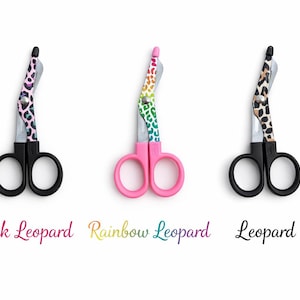 May include: Three medical shears with black handles and blades. The shears have colorful leopard print designs on the handles. The text below the shears reads "Pink Leopard", "Rainbow Leopard", and "Leopard".